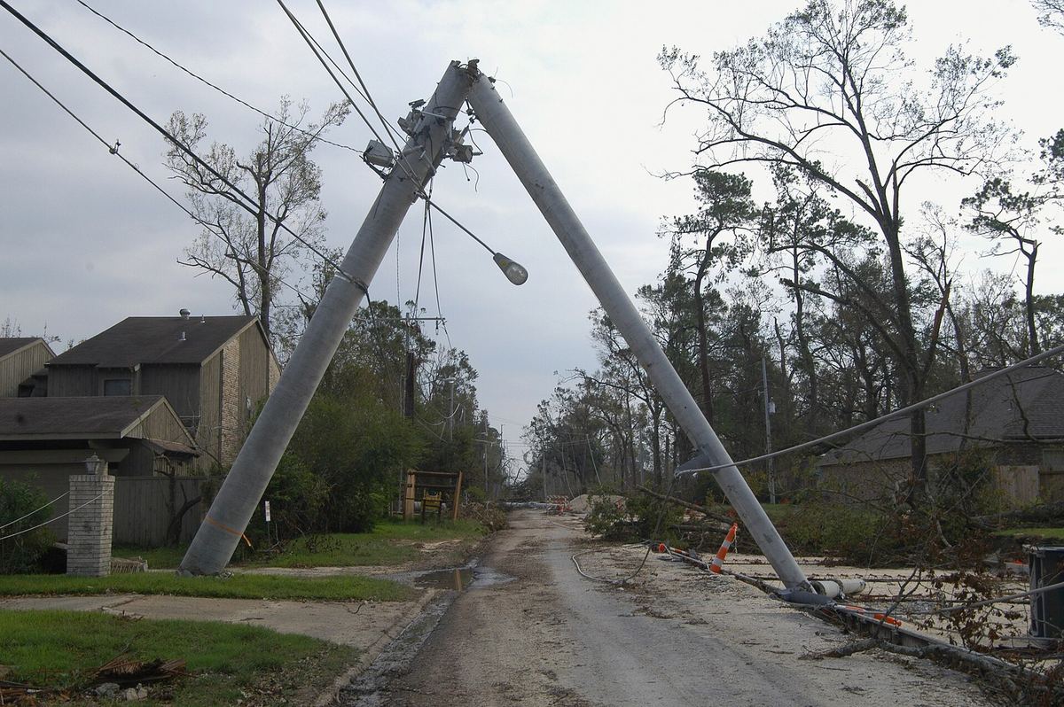 A snapped power pole leaning over a neighborhood street, with wires down
